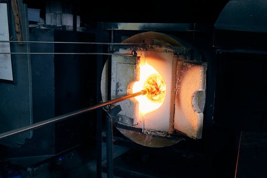 A glass bowl on a punti goes into a hot, orange glory hole.